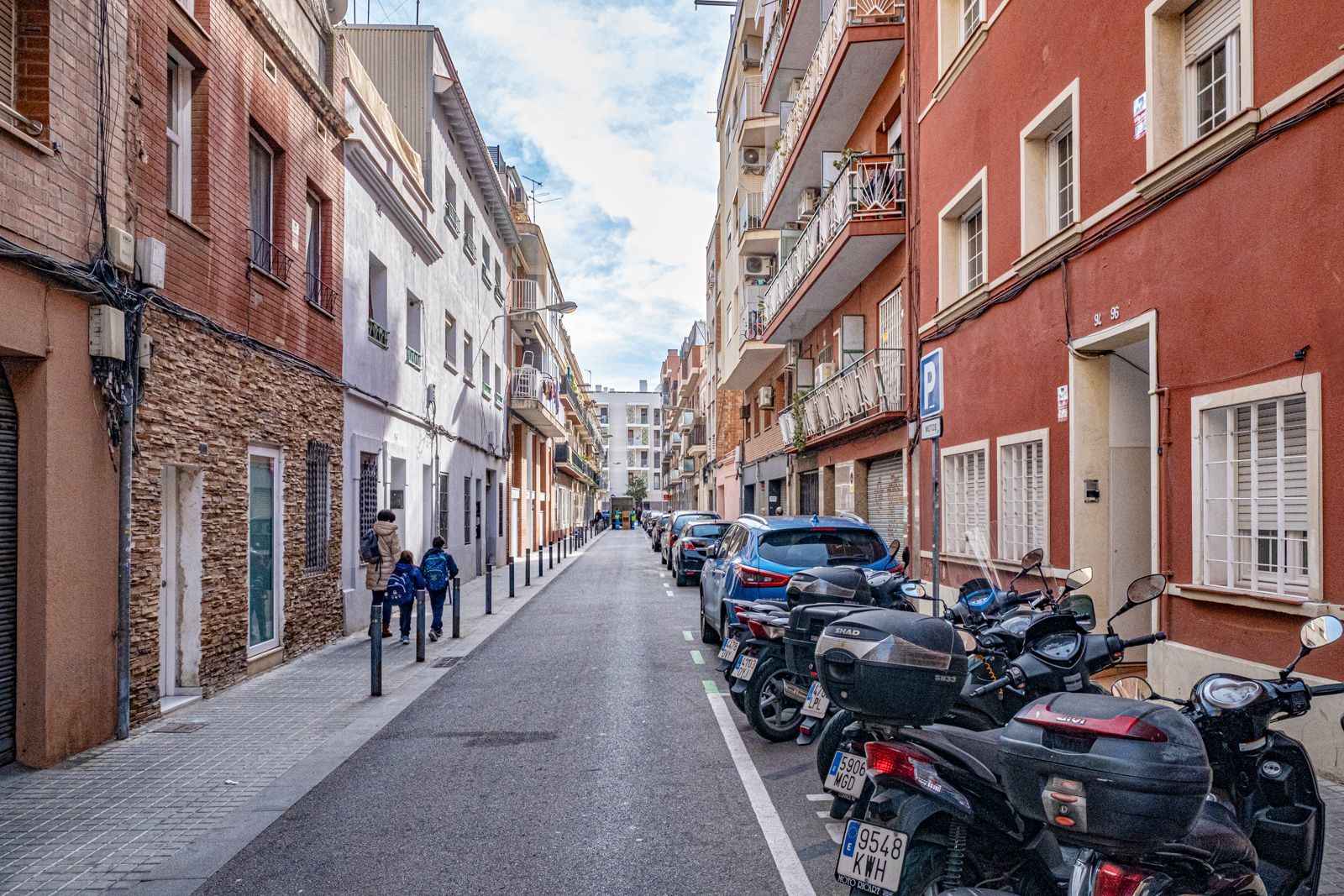 A row of motorcycles are parked on the side of a narrow street.