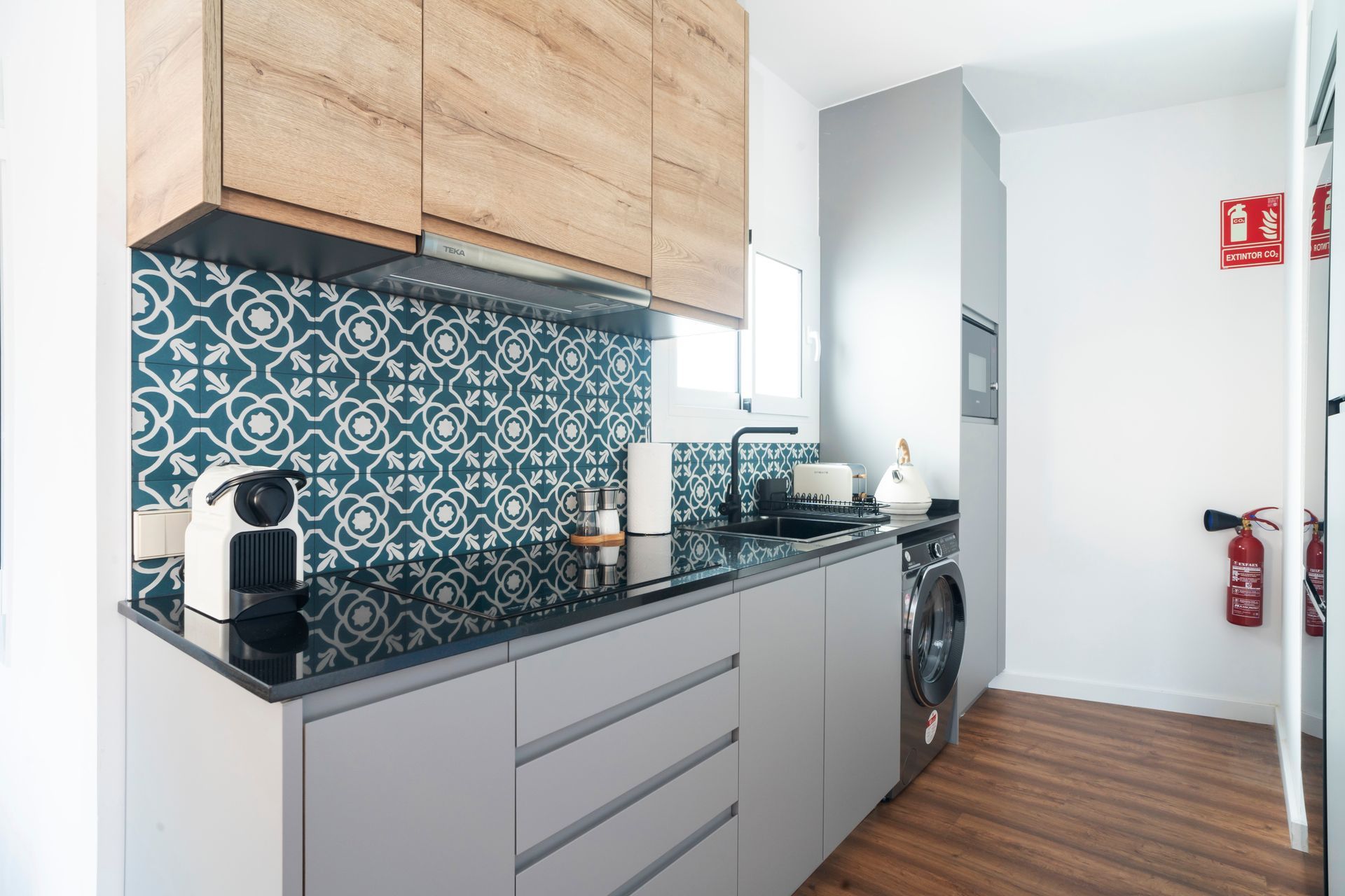 A kitchen with a stove top oven , a washer and dryer , and a fire extinguisher.