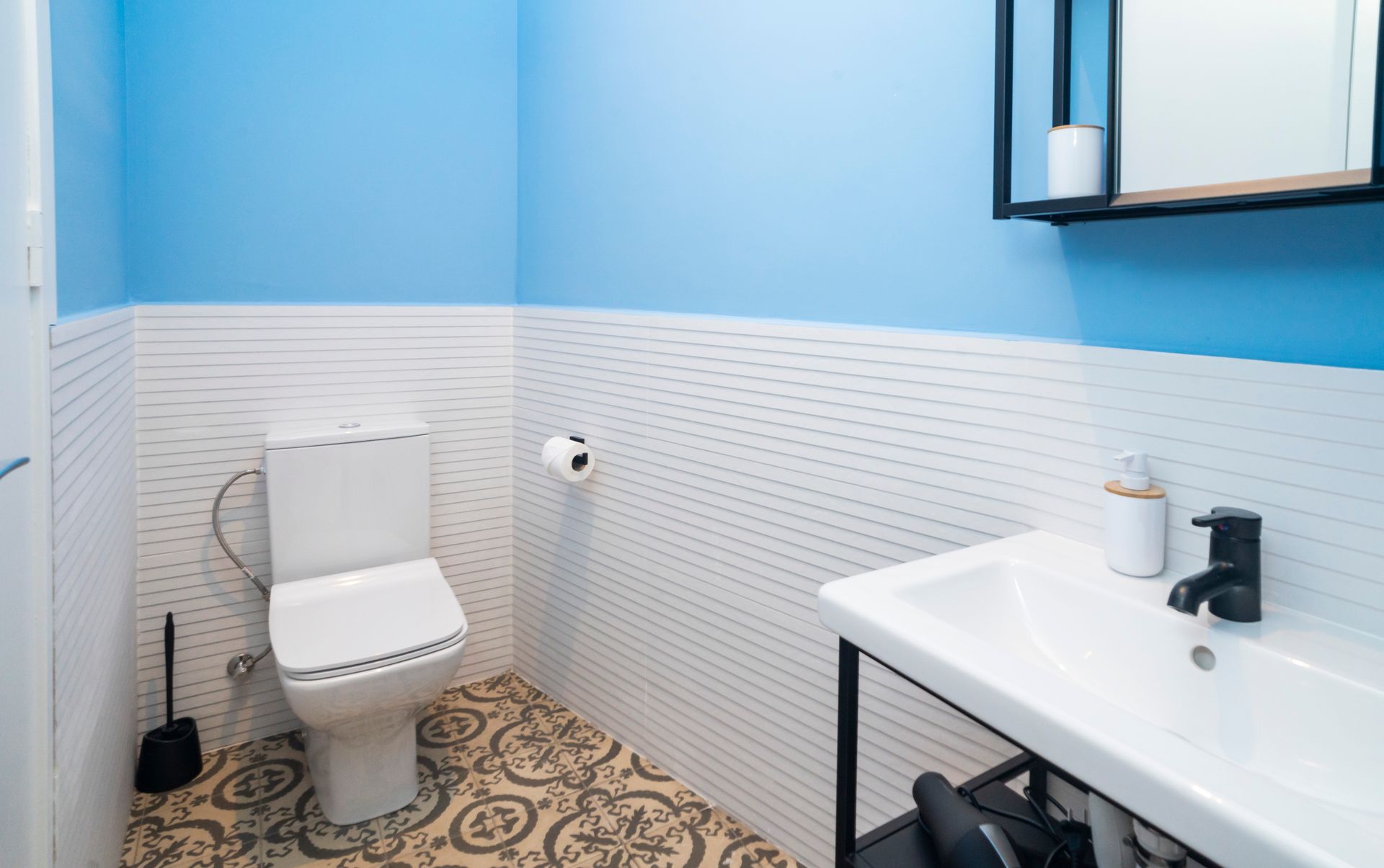 A bathroom with a toilet , sink , mirror and blue walls.