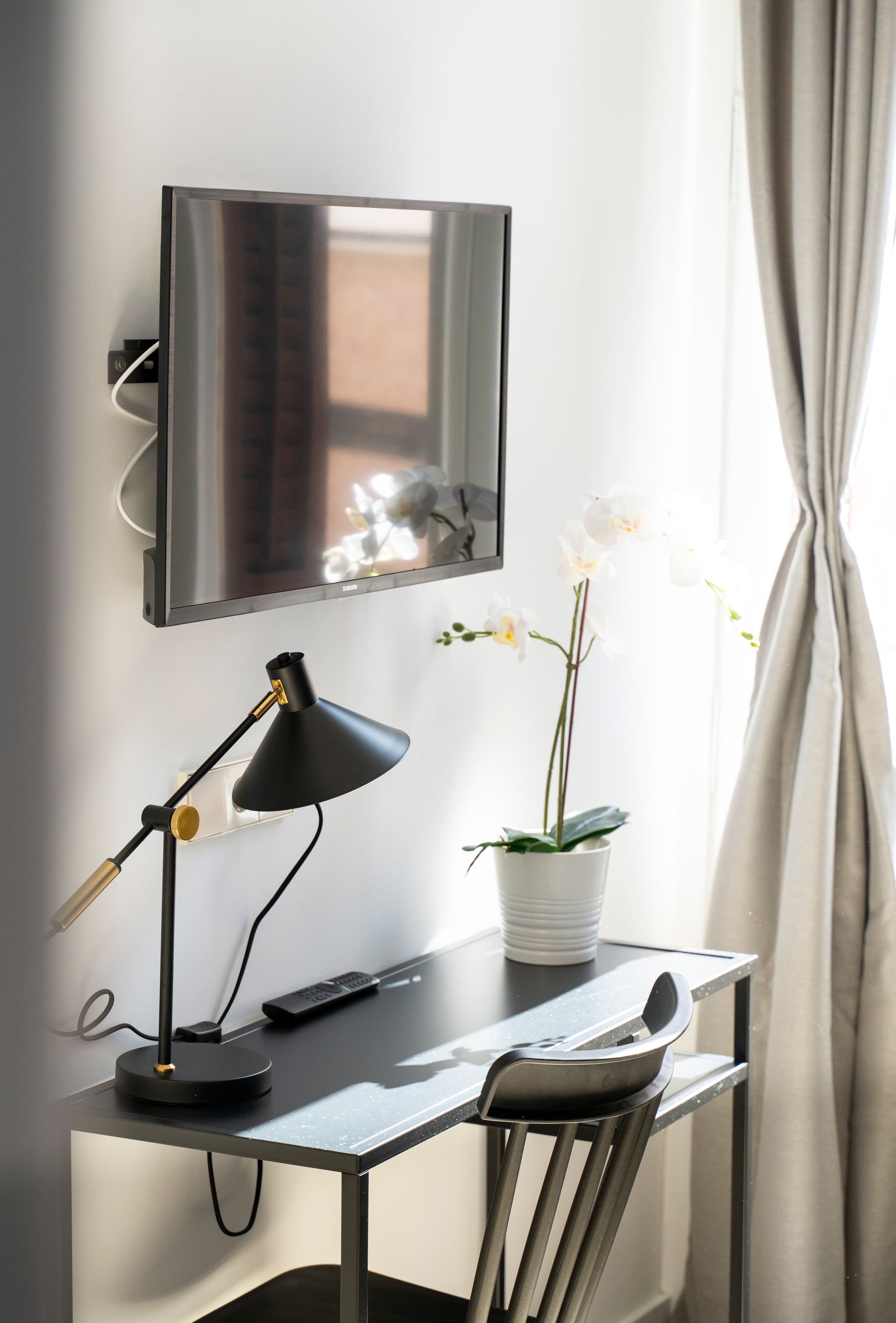 A desk with a lamp and a flat screen tv on the wall.