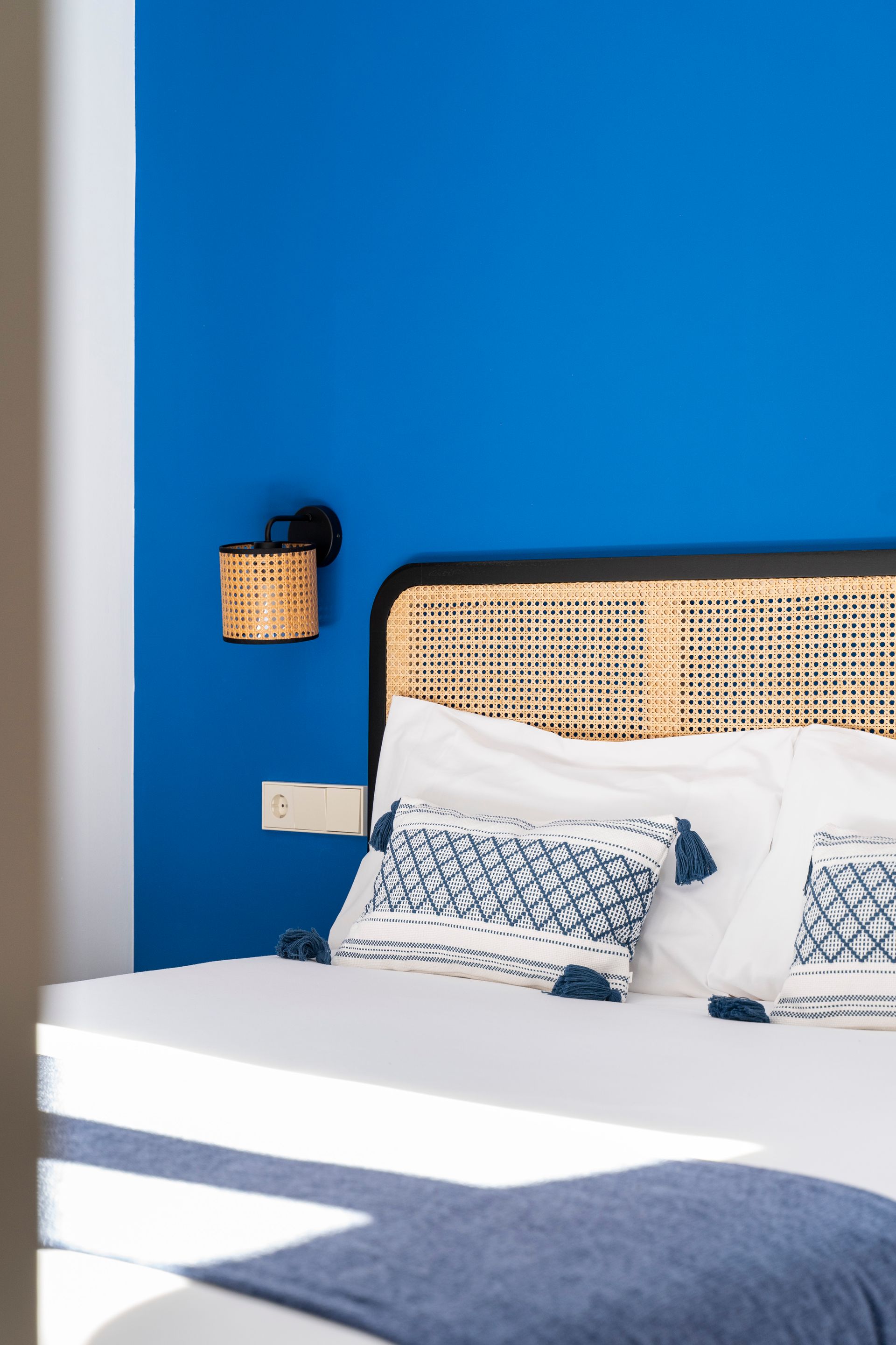 A bed with a wicker headboard in a bedroom with a blue wall.