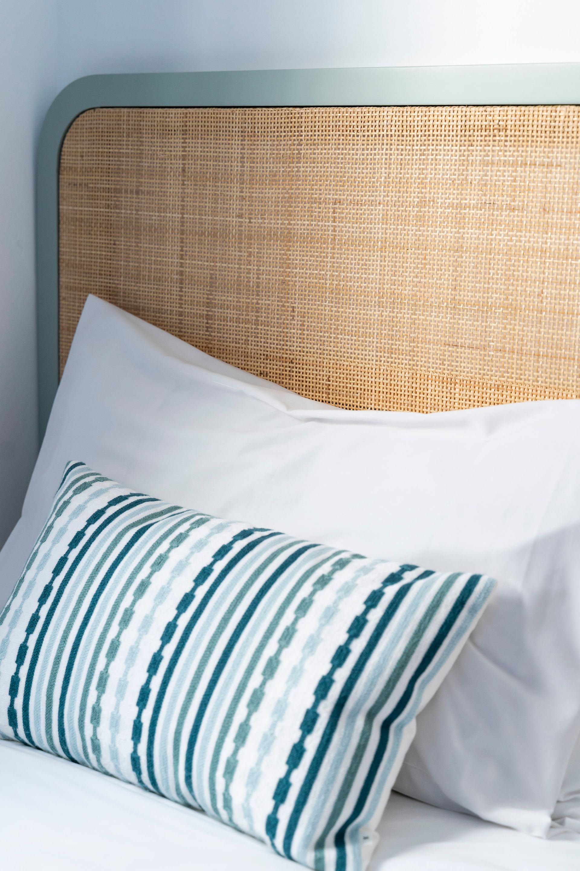 A bed with a wicker headboard and striped pillows.