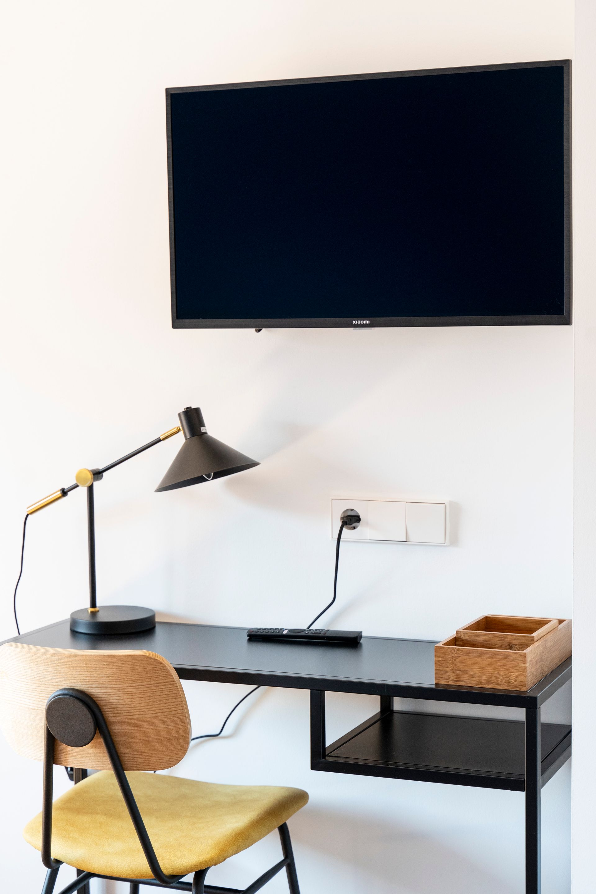 A desk with a chair , lamp and television on the wall.