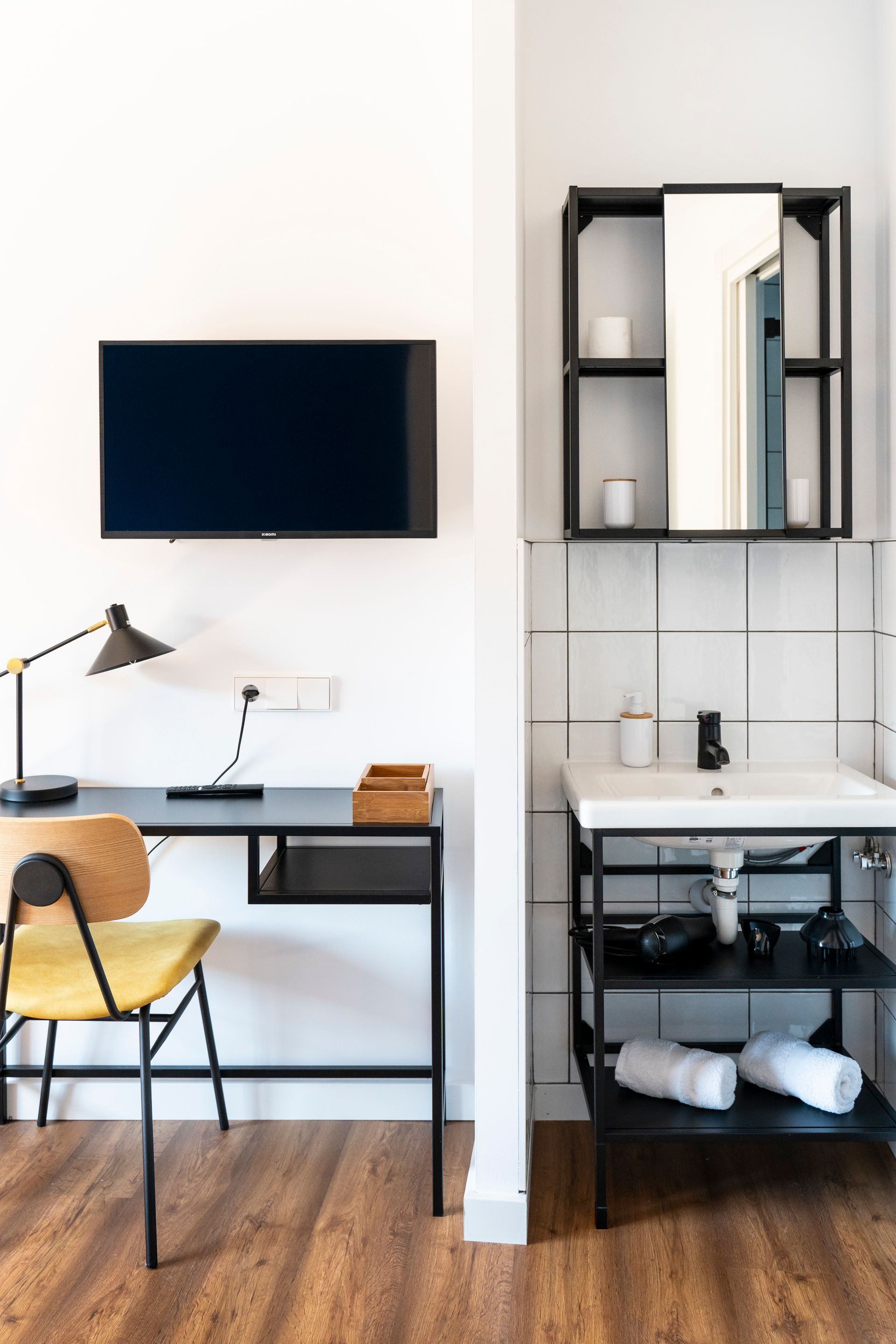 A room with a desk , chair , television , sink and mirror.