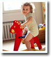 A little girl is sitting on a red rocking horse.