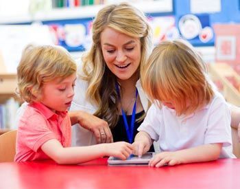 A woman is teaching two young children how to use a tablet computer.