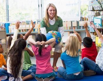 A teacher is holding a globe in front of a group of children