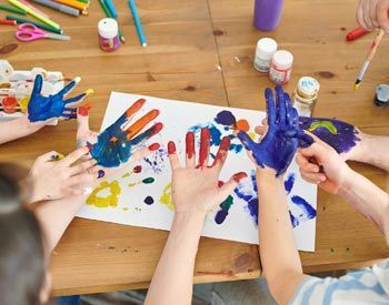 A group of children are painting their hands on a piece of paper.