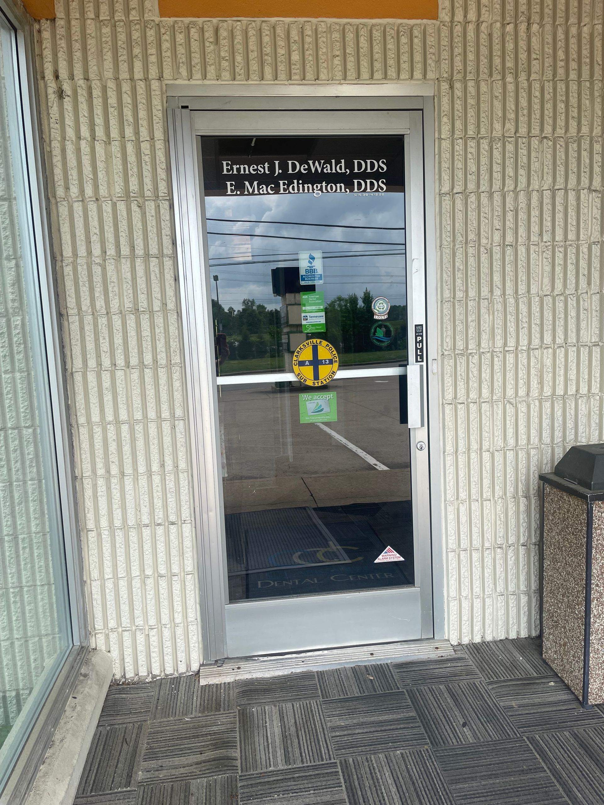 A brick building with a glass door and a trash can in front of it.