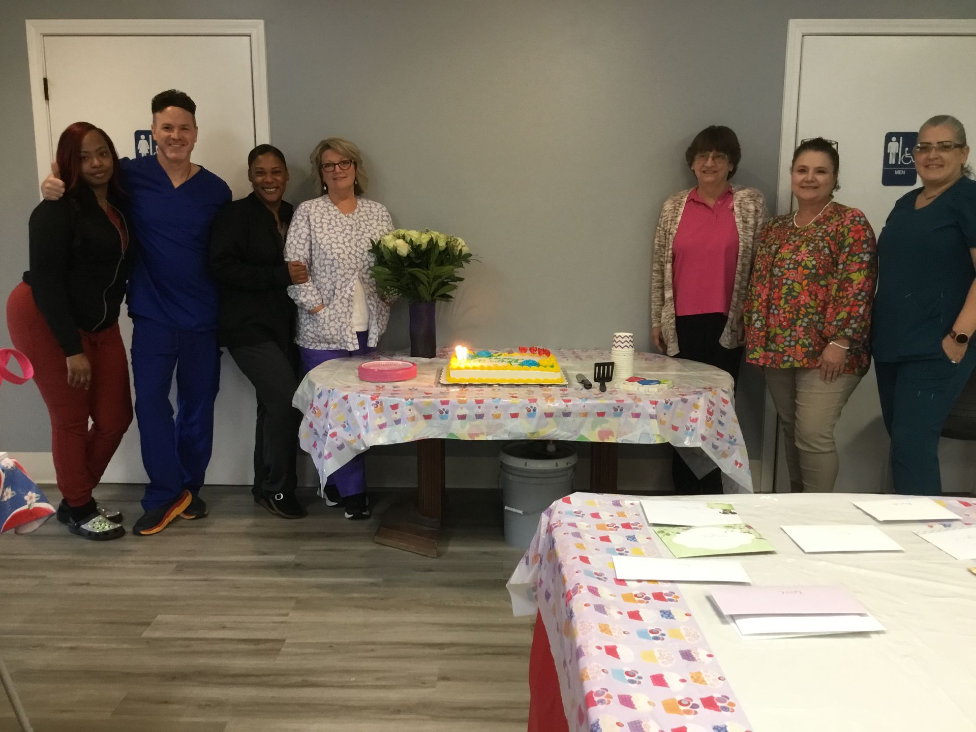 A group of people are standing around a table with a cake on it.