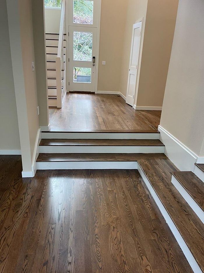A hallway with hardwood floors and white stairs leading to a door.