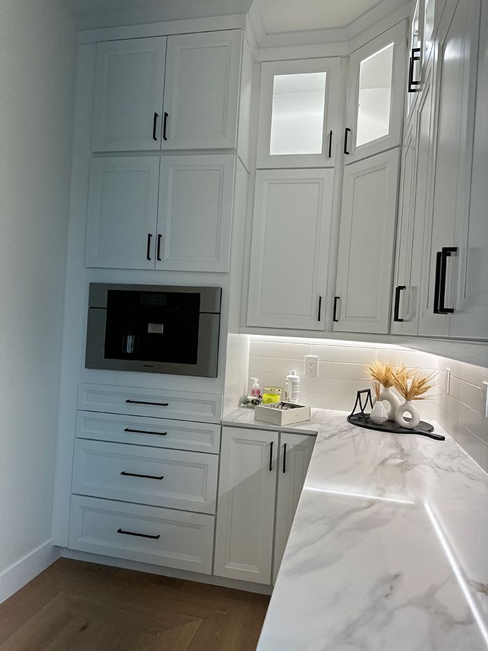 A kitchen with white cabinets , marble counter tops , and a microwave.