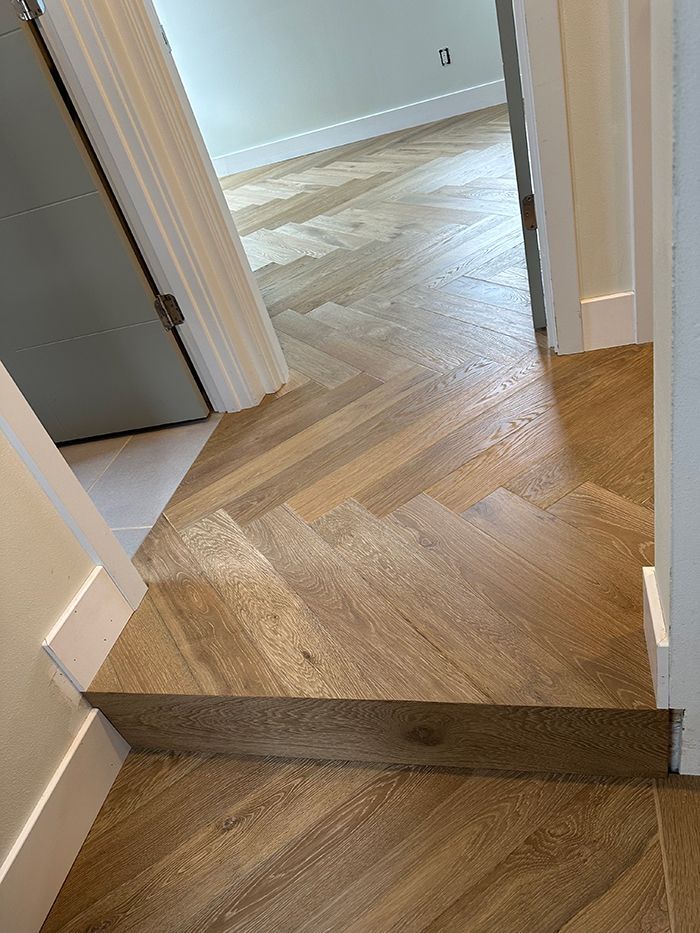 A wooden floor with a herringbone pattern in a hallway leading to a bedroom.
