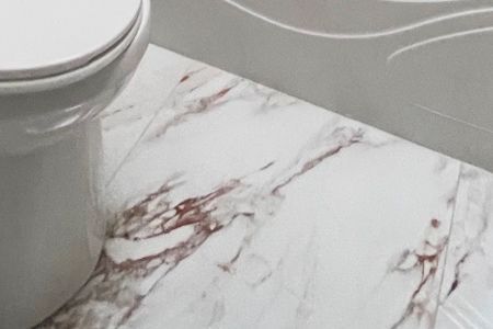 A toilet is sitting on a marble floor next to a bathtub.