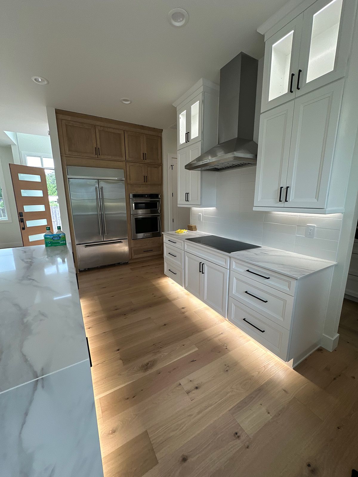 A kitchen with white cabinets , wooden floors , stainless steel appliances and a stove top oven.
