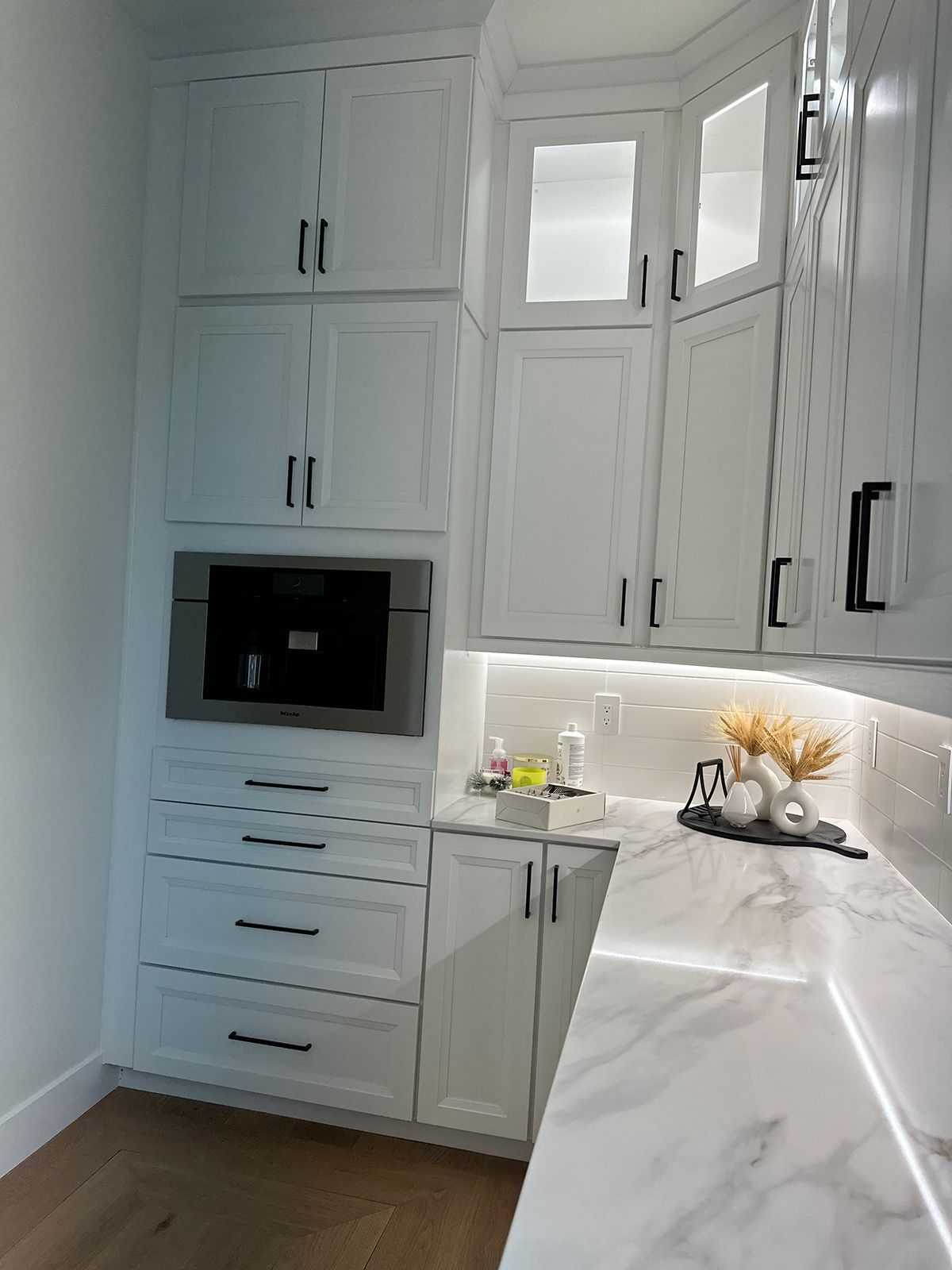 A kitchen with white cabinets and marble counter tops.