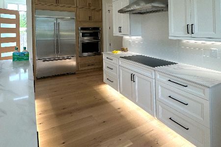 A kitchen with white cabinets , stainless steel appliances , and hardwood floors.
