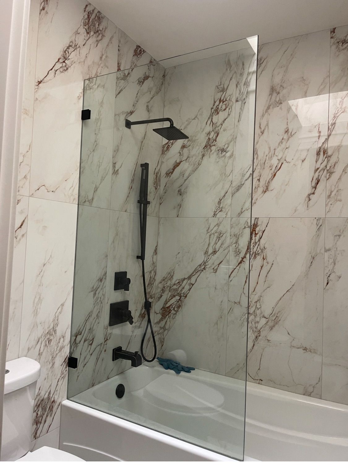 A bathroom with marble walls and a bathtub with a glass shower door.