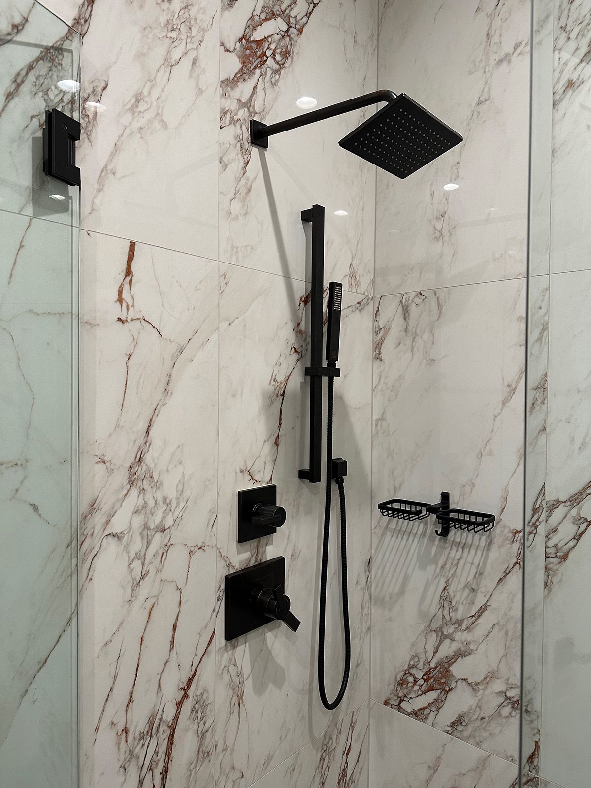 A shower with a black shower head and a marble wall
