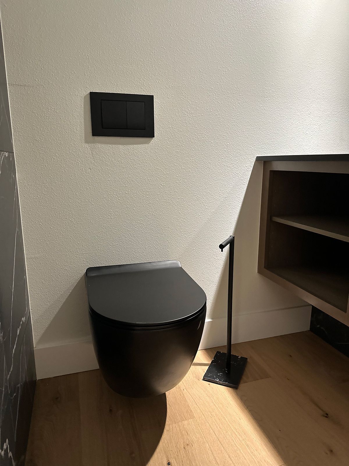 A black toilet is sitting on a wooden floor in a bathroom.