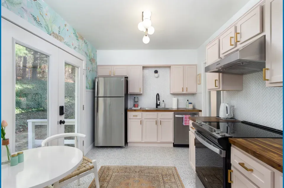 Kitchen with light pink cabinets, stainless steel appliances, and a round table next to the door.
