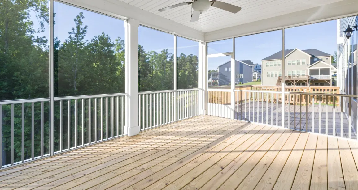 Screened porch with white railings and wooden floor, overlooking trees and houses.