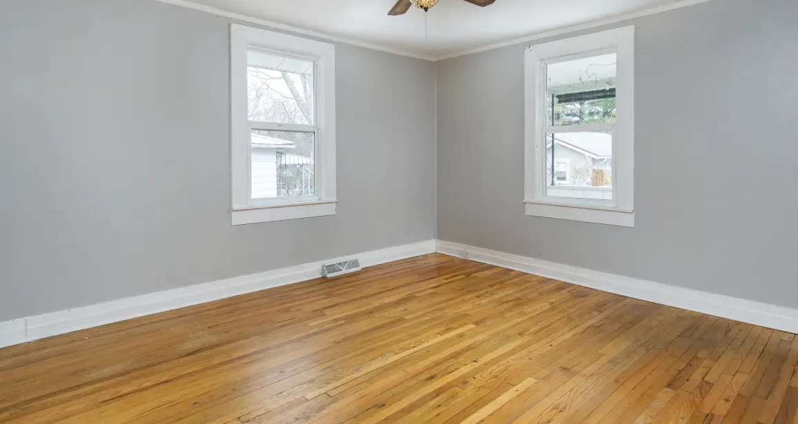 Empty room with hardwood floors, gray walls, white trim, and two windows.
