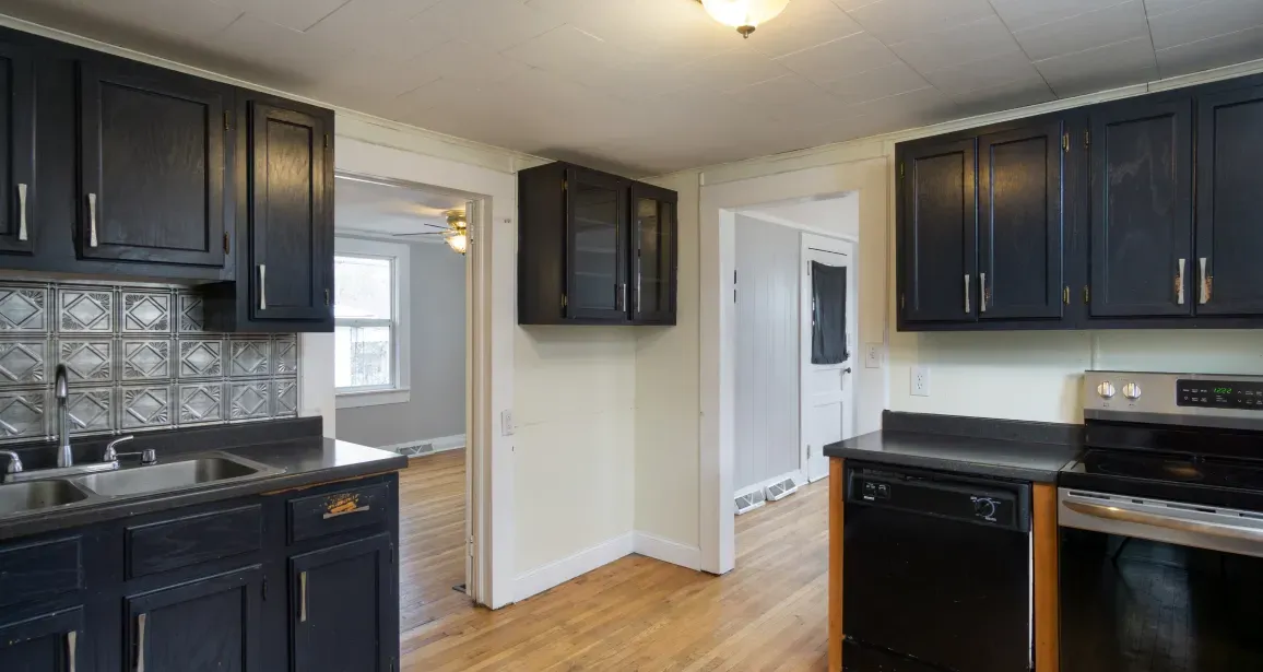 Kitchen with dark blue cabinets, black countertops, and stainless steel appliances; doorway to another room.