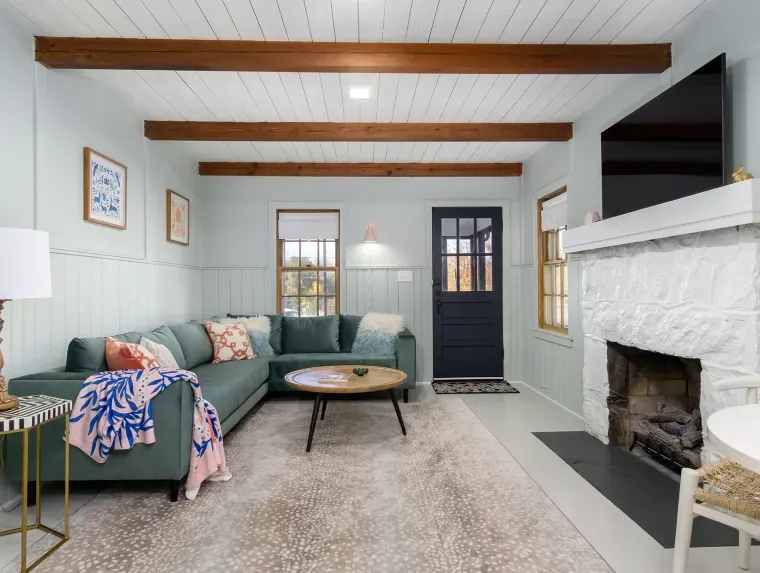 Living room with teal sofa, white fireplace, and wooden ceiling beams.