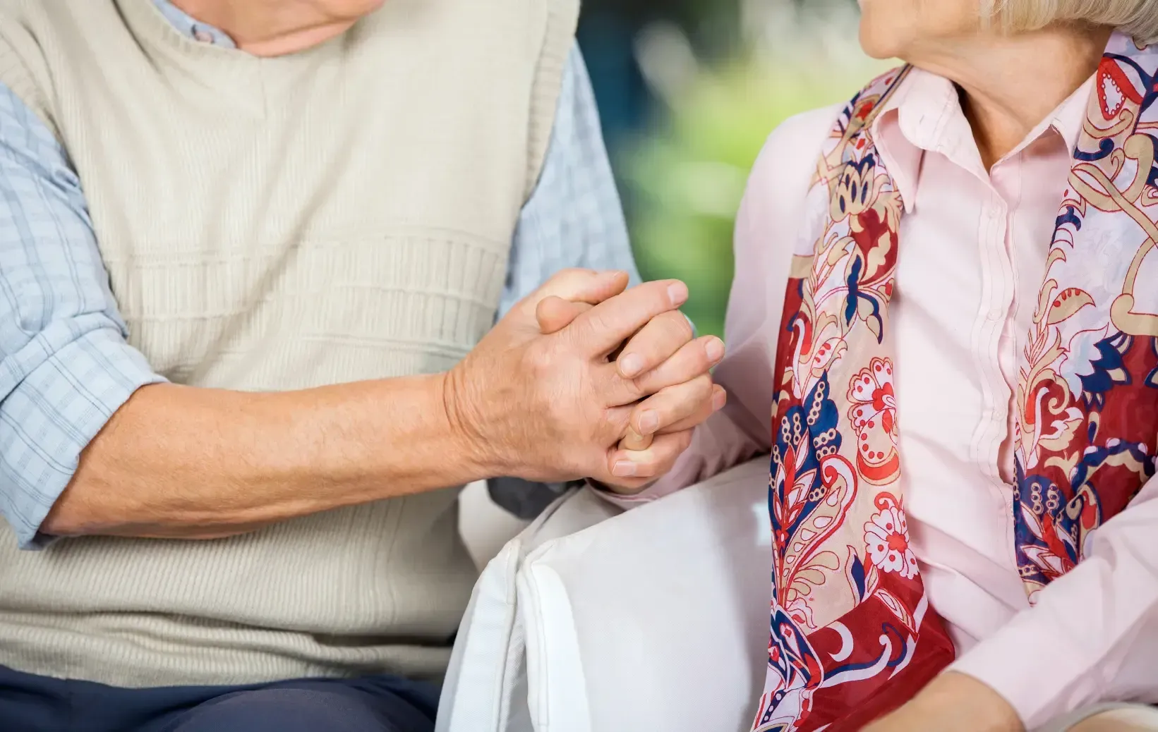 An elderly couple is holding hands while sitting in a chair.
