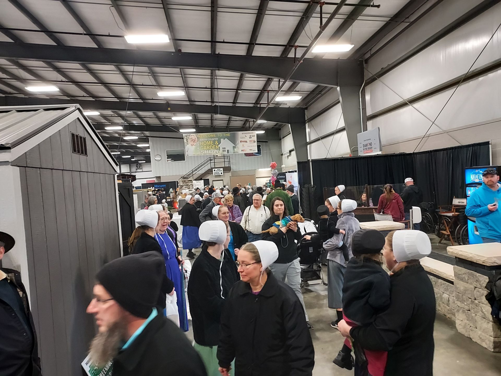 People, some wearing bonnets, at a large indoor event, possibly a market or auction.