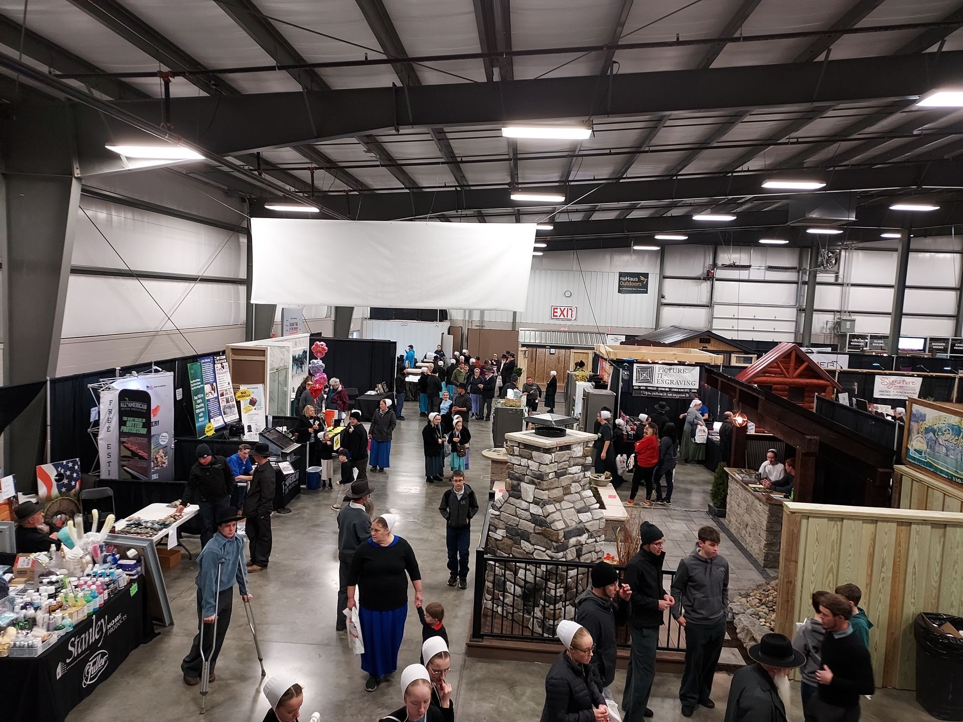 Large indoor event with many people browsing booths, likely a market or fair.