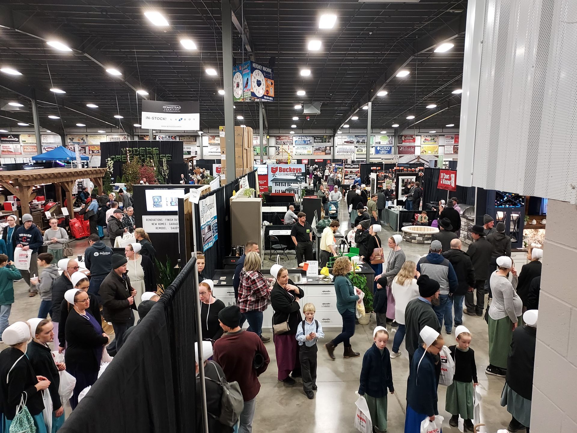 Large indoor event with many people browsing booths, including those dressed in plain clothing.