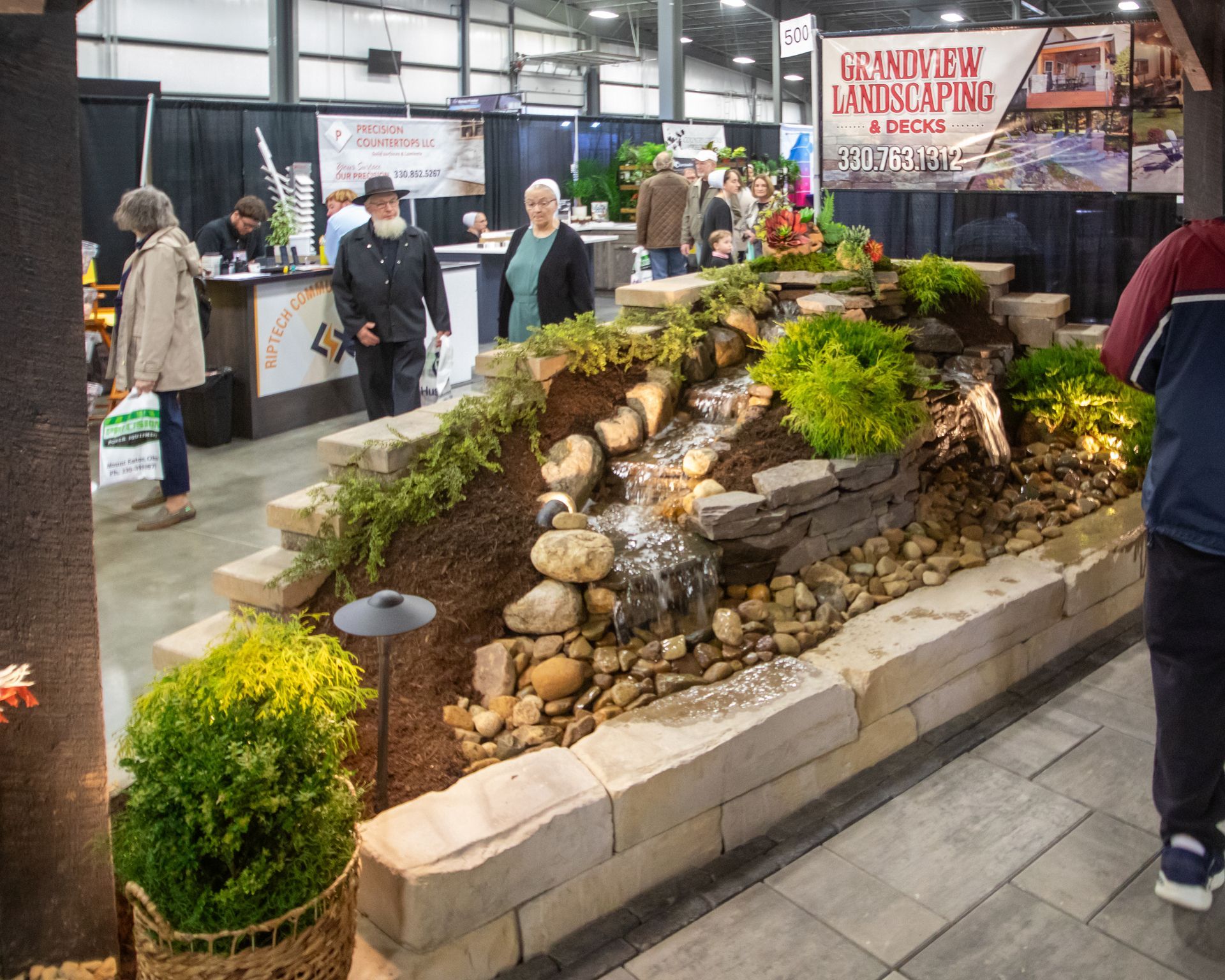Plant display at an indoor event, featuring various greenery on green turf with a sign.
