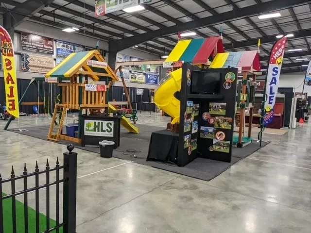 Playground set display with slide and swing set at an indoor event with sale signage.