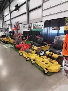 Lawn mowers displayed at a trade show booth, various sizes and colors, inside a large building.