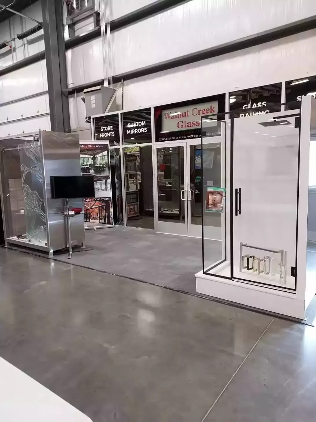 A showroom with shower displays, entrance doors, and a TV screen. Gray and white colors dominate the space.