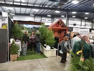 Trade show booth with log cabin, trees, and people.