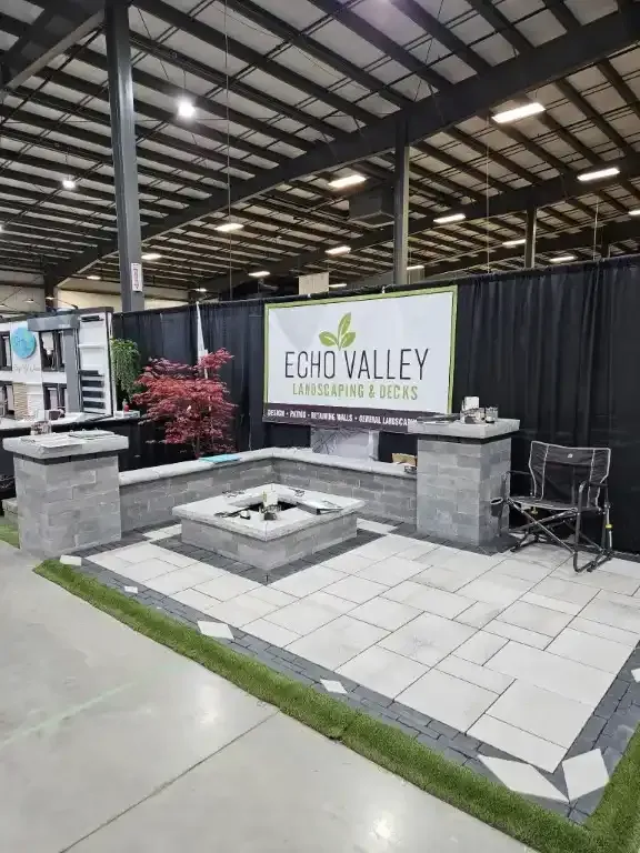 Outdoor living space display by Echo Valley Landscape & Rock. Features a fire pit, patio pavers, and retaining walls.