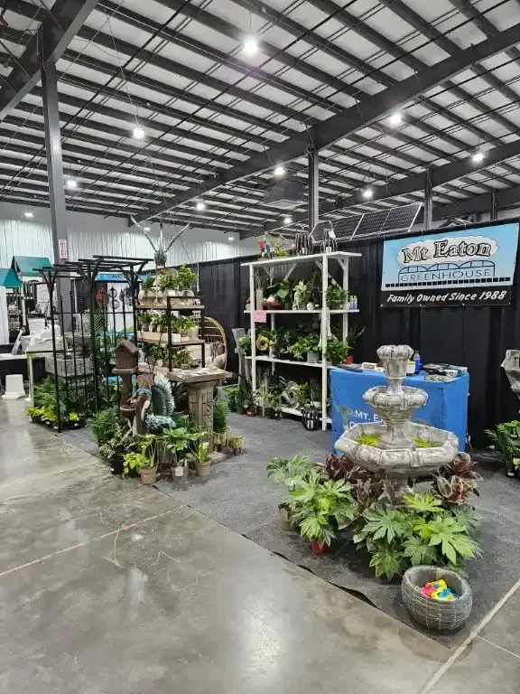 Indoor plant display with tiered shelves, fountain, and vendor sign.