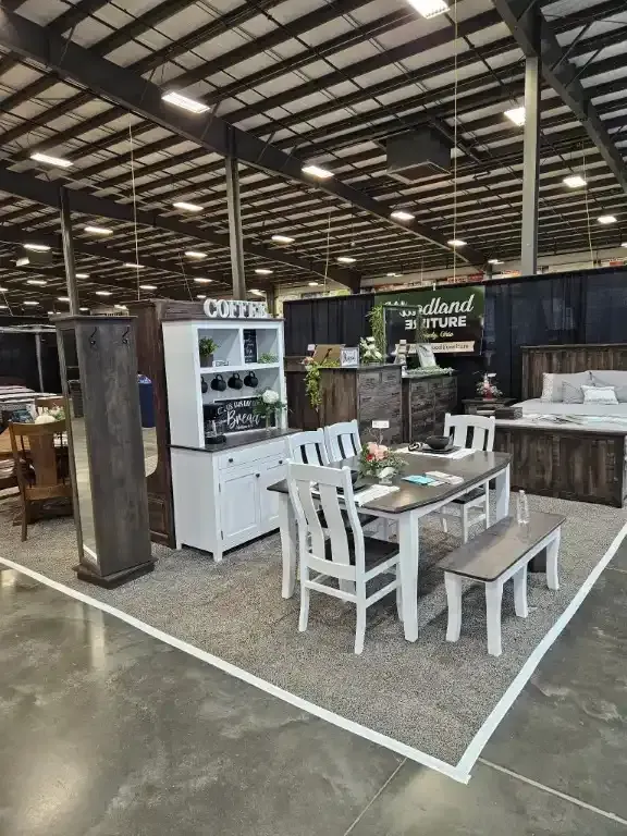 Furniture display at an event. Dining set with white chairs, bench, table. White hutch with coffee sign.
