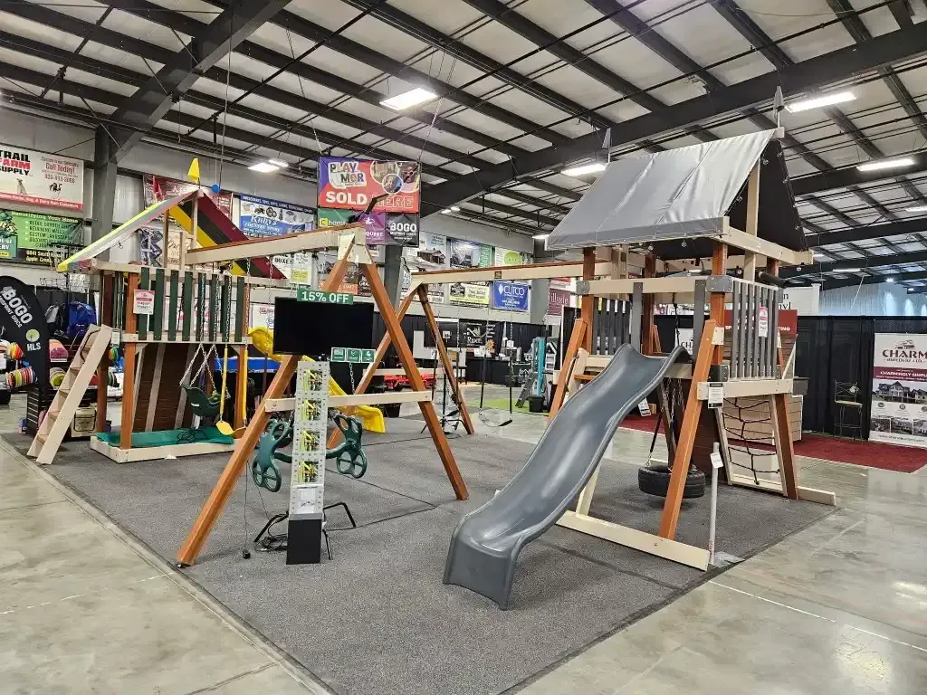 Playground set display inside a large building, featuring swings, a slide, and a climbing structure.