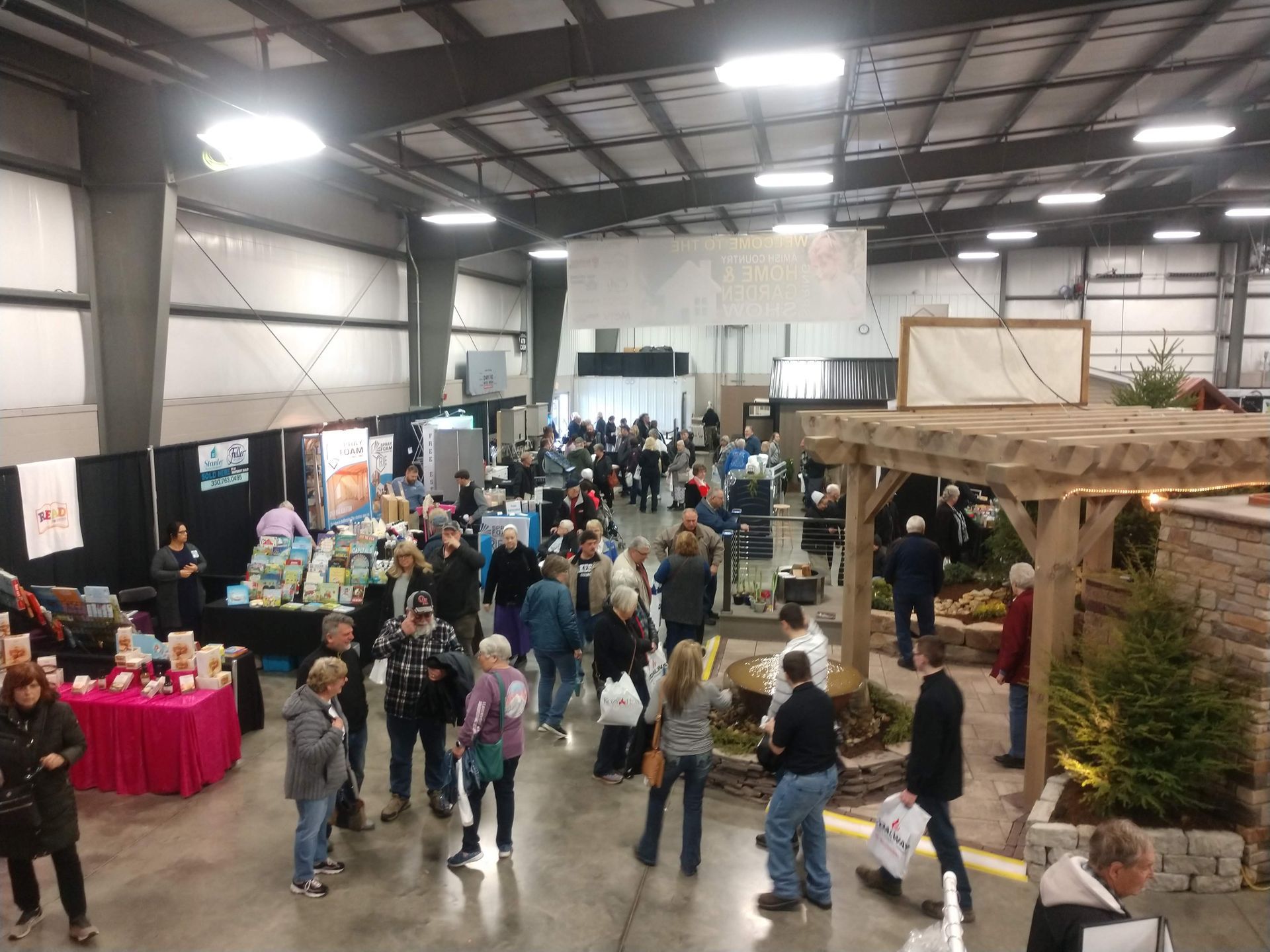 Large indoor event with many people browsing booths, displays, and a small garden structure.