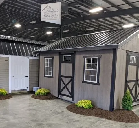Display of sheds with gray siding, black roofs and trim, set on simulated landscaping.