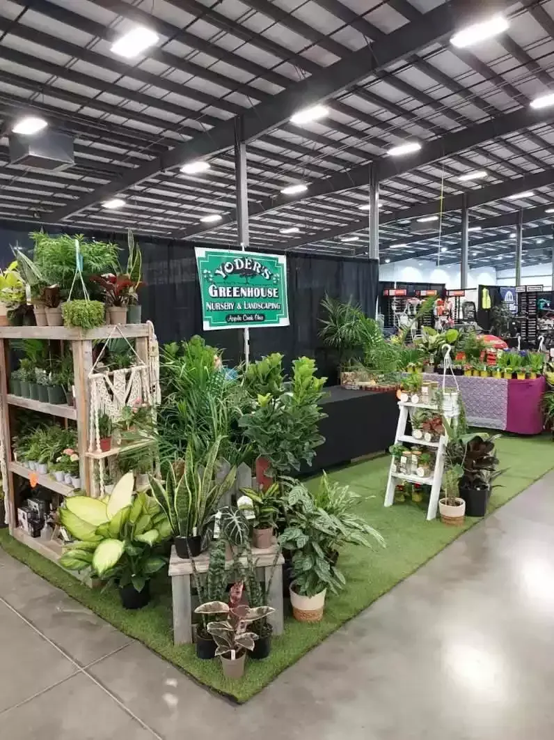 Plant display at an indoor event, featuring various greenery on green turf with a sign.