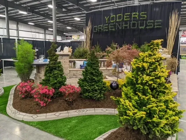 A garden display by Yoder's Greenhouse featuring various plants and landscaping elements at an exhibition.