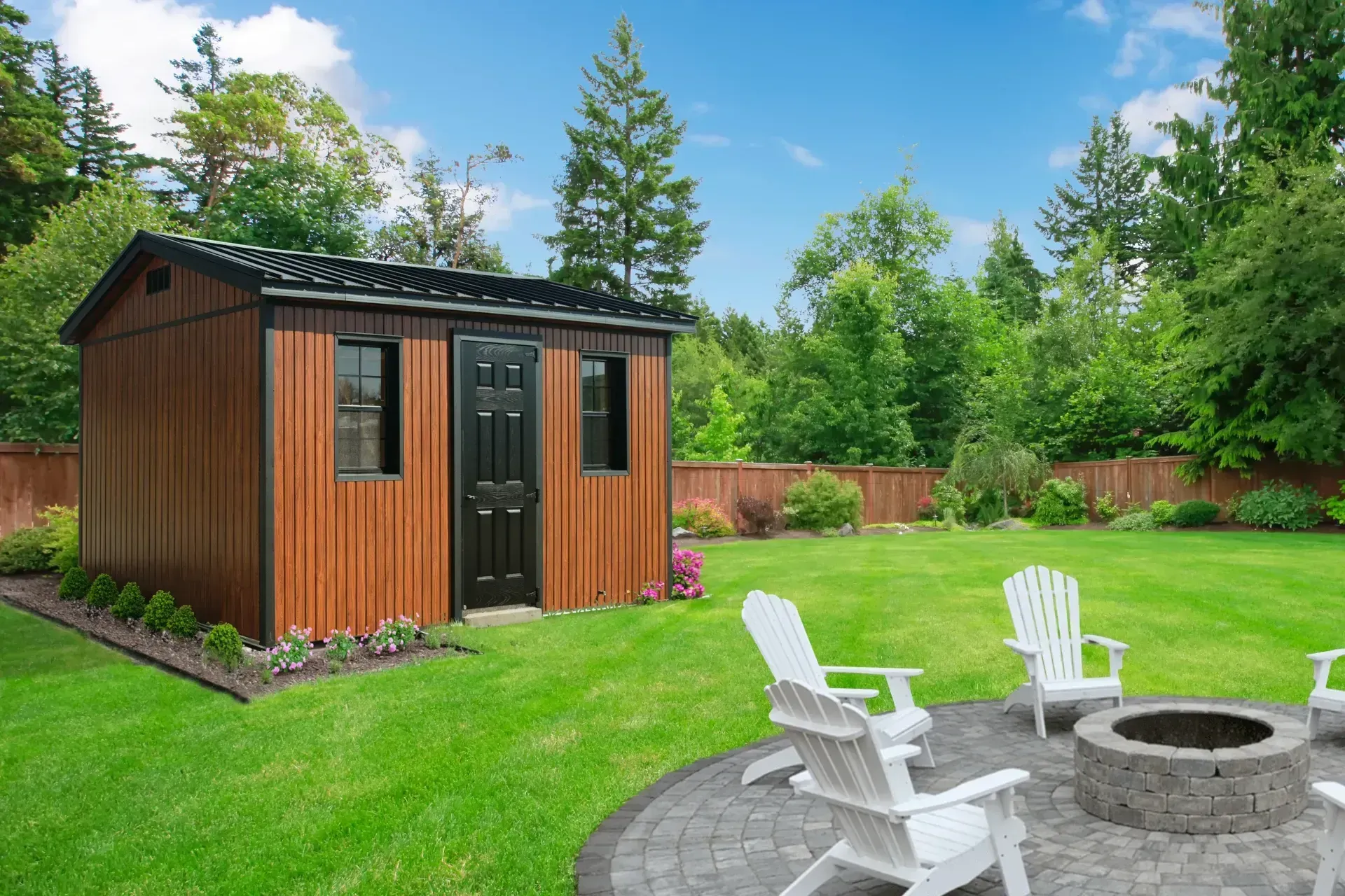 Brown shed with black door and windows in a backyard with a fire pit and white chairs.