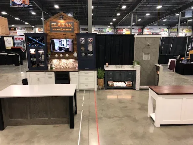 Trade show booth with kitchen and bathroom displays; white and blue cabinetry, a TV, and countertops.