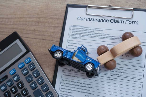 Car insurance claim form with toy cars and calculator on wooden desk.