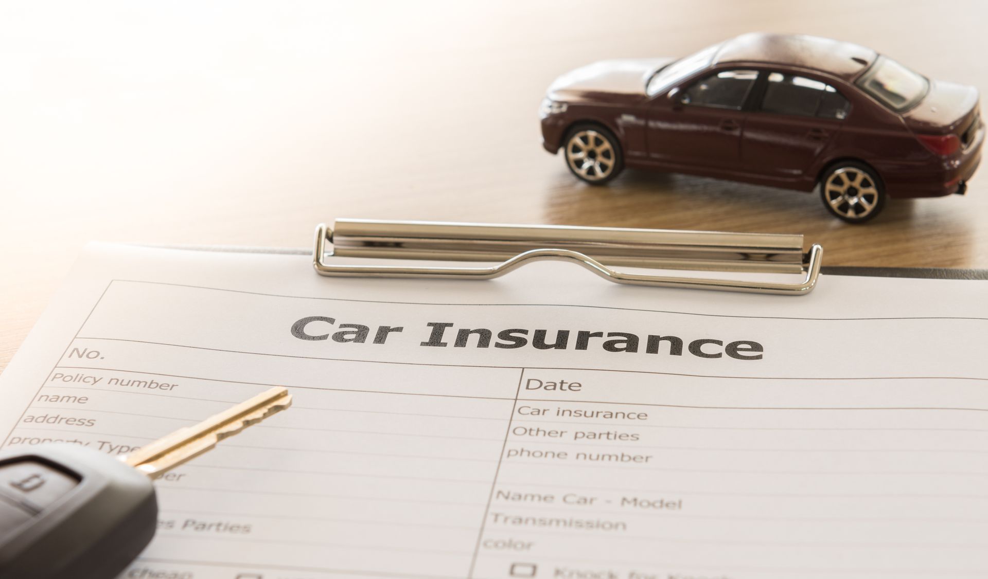 Close-up of a car insurance application form with a dark car model and key remote on desk.